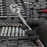 Gloved hand holding a chrome ratchet above the open IRONVOLT 218-piece tool set.